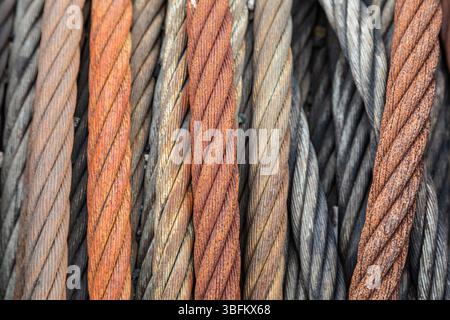 Gros plan de câbles métalliques fortement rouillés enroulés sur une vieille bobine, soulignant la texture et la corrosion dans un chantier naval abandonné. Banque D'Images