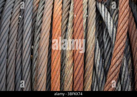 Gros plan de câbles métalliques fortement rouillés enroulés sur une vieille bobine, soulignant la texture et la corrosion dans un chantier naval abandonné. Banque D'Images