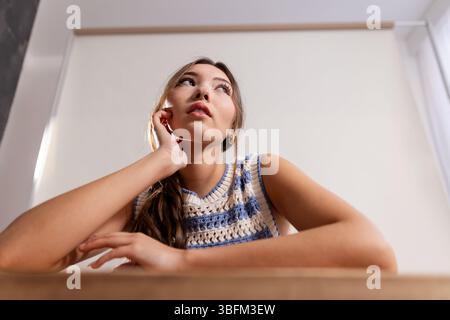 Portrait en studio en angle bas d'une jeune femme adulte assise à une table, regardant hors du cadre tout en penchant les deux bras sur la table, son visage reposant contre Banque D'Images