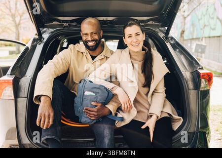 Portrait d'un couple multiracial heureux assis ensemble dans le coffre de voiture Banque D'Images