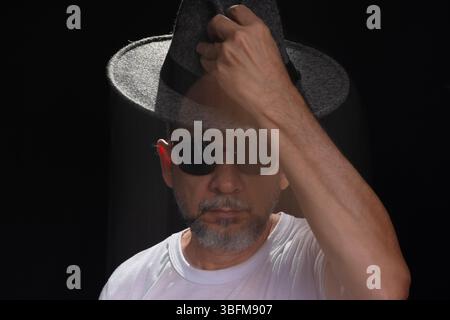 Portrait artistique de l'homme chauve barbu en chemise blanche faisant flou de mouvement avec les bras et les mains. Fond noir. Banque D'Images