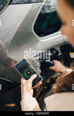 Au-dessus de la vue de l'épaule de la femme en utilisant l'application mobile tout en chargeant la voiture électrique Banque D'Images