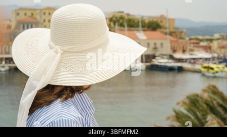 Femme portant un chapeau d'été profitant de la vue sur les bateaux et les bâtiments du front de mer à chania, crète Banque D'Images