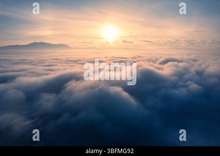 Vue aérienne du lever de soleil doré brille sur la mer de brouillard et montagne lointaine sous le ciel serein Banque D'Images