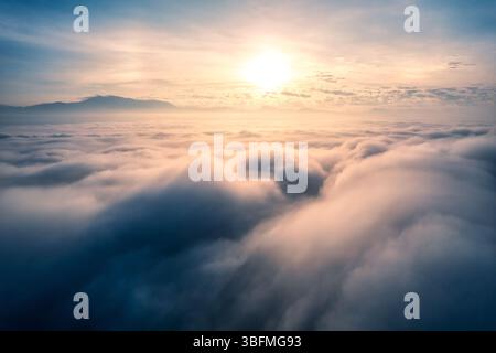 Vue aérienne du lever de soleil doré brille sur la mer de brouillard et montagne lointaine sous le ciel serein Banque D'Images