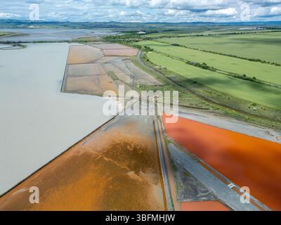 Vue aérienne de marais salants colorés près de Burgas, Bulgarie. Les bassins d'évaporation rouge et orange éclatants contrastent avec les amas de sel blanc et la mer turquoise Banque D'Images