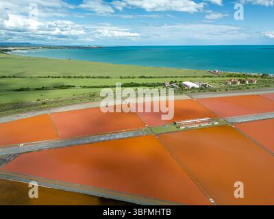 Vue aérienne de marais salants colorés près de Burgas, Bulgarie. Les bassins d'évaporation rouge et orange éclatants contrastent avec les amas de sel blanc et la mer turquoise Banque D'Images