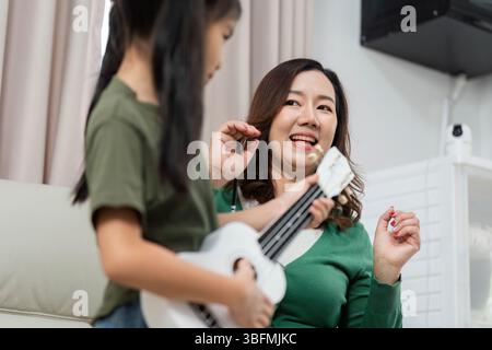 Joyeux moments musicaux. Une mère et sa fille partagent le rire en jouant du ukulélé. Banque D'Images