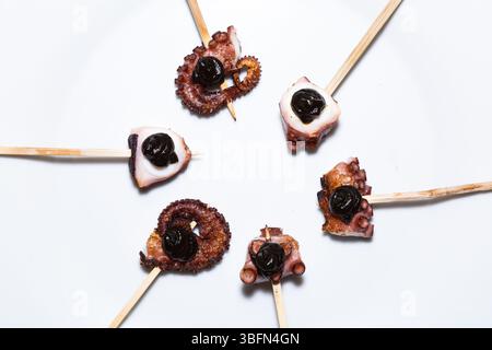 Des brochettes de poulpe grillées à l'aïoli noir à l'ail sont présentées sur une assiette blanche, offrant un savoureux apéritif. Banque D'Images