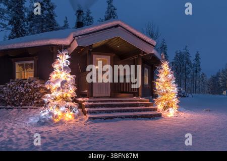 Retrouvez le cœur de la magie hivernale dans ce cadre idyllique de Noël en Laponie. Une lumière chaleureuse de la cabine vous invite à partir d'un paysage tranquille et enneigé. Banque D'Images