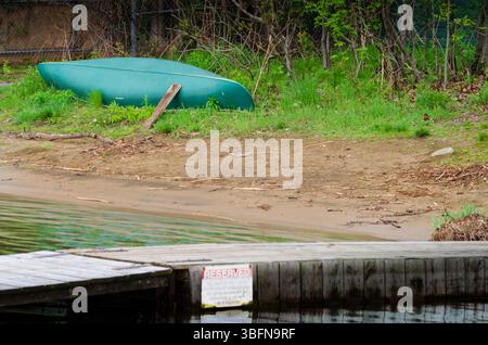 Canot vert reposant à l'envers sur l'herbe près d'une plage et d'un quai Banque D'Images