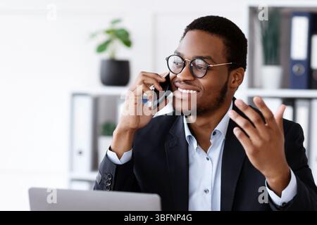 Un entrepreneur afro-américain souriant ayant une conversation téléphonique au bureau Banque D'Images