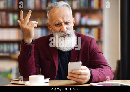 Homme senior en colère utilisant un téléphone portable dans un café Banque D'Images