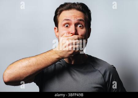 L'homme couvre la bouche avec sa main pour ne pas parler, portrait sur fond blanc Banque D'Images