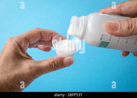 Femme versant un médicament liquide ou un antiacide sur la tasse. Vue rapprochée. Banque D'Images