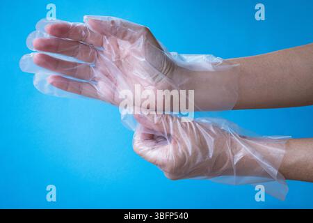 Main de femme portant des gants en plastique. Vue rapprochée, isolée sur fond bleu. Banque D'Images