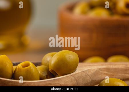 Les olives vertes sont disposées dans une cuillère en bois, avec un bol de plus d'olives en arrière-plan. Le cadre est chaleureux et rustique, idéal pour une Méditerranée-i. Banque D'Images