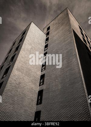 Ce bâtiment saisissant arbore des formes géométriques uniques et des briques complexes, s'élevant haut sur un ciel sombre dans un cadre urbain contemporain. Banque D'Images