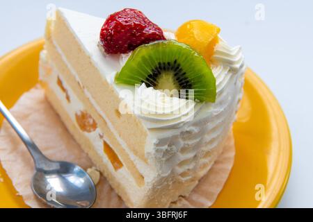Gros plan d'une tranche de gâteau à la crème de fruits avec fraise, pêche et kiwi isolé sur blanc. Banque D'Images