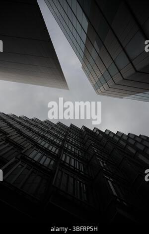 Une vue spectaculaire vers le haut des gratte-ciels modernes de Londres, avec des façades en verre sombre et des lignes angulaires sous un ciel sombre et couvert. Banque D'Images