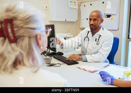 Médecin expliquant les résultats médicaux sur ordinateur à un patient senior hospitalisé Banque D'Images