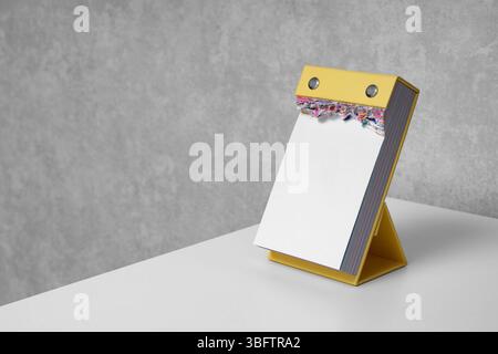 Calendrier à déchirer vertical vierge avec des pages déchirées sur un bureau blanc. Maquette. Vie au bureau. Planification, productivité, fournitures de bureau, journalisation, rédaction Banque D'Images