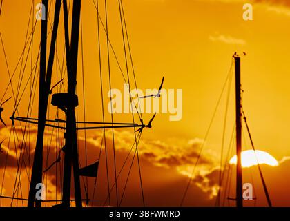 Le soleil se couchant dans un beau ciel orange derrière des nuages avec les mâts de voiliers et mouettes lors d'une soirée d'été à Marsh Harbor des Bahamas. Banque D'Images