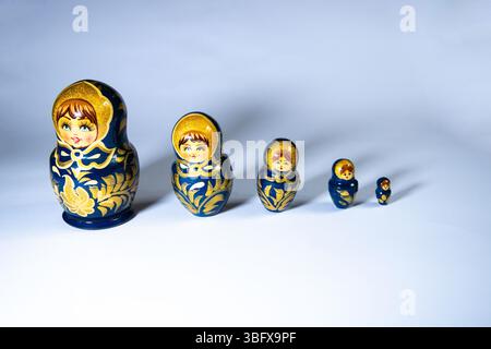 Cinq poupées de nidification russes bleues et dorées disposées en ligne sur un fond blanc, mettant en valeur la conception traditionnelle de l'art populaire. Banque D'Images