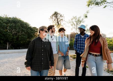 Groupe multiracial de jeunes marchant et parlant ensemble dans la ville au coucher du soleil. Amitié, inclusion et mode de vie décontracté en plein air. Banque D'Images