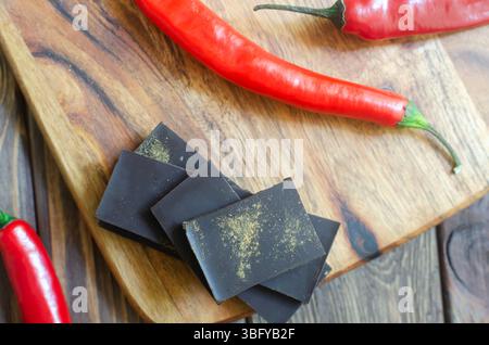 Morceaux de chocolat noir extra avec trois piments rouges sur une planche à découper en bois sur la table. Concept alimentaire tendance. Mise au point sélective. Horizontal ou Banque D'Images