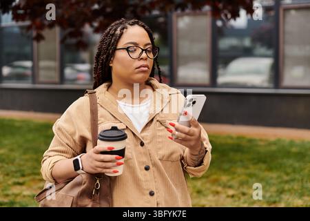 Une professeure d'université vérifie son téléphone avec un café dans un cadre extérieur détendu. Banque D'Images