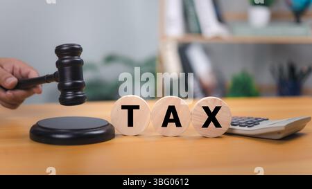 Marteau en bois et le mot TAXE sur les blocs ronds sur un bureau en bois, symbolisant le droit fiscal, le jugement juridique, les décisions financières, avec une calculatrice dans le bac Banque D'Images