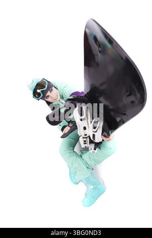 Image verticale, isolée sur blanc, jolie femme caucasienne en tenue de ski violette, lunettes de ski bleues et pantalon bleu assis jambes croisées et tenir bla Banque D'Images