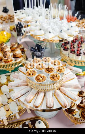 Service traiteur présentant de délicieux desserts comme des gâteaux, des éclairs, des tartes, des mousses et des pâtisseries sur des plateaux dorés lors d’une fête Banque D'Images