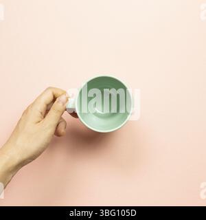 Femme main tenant une tasse vide verte sur fond rose. Vue du dessus Banque D'Images