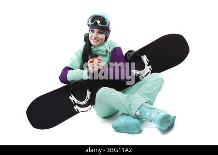 Image verticale, isolée sur blanc, jolie femme caucasienne en tenue de ski violette, lunettes de ski bleues et pantalon bleu assis jambes croisées et tenir bla Banque D'Images