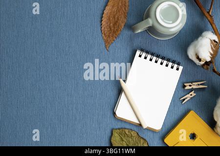 Lieu de travail et d'étude. Concept d'hiver. Carnet et crayon, tasse à café, plante sèche sur fond de tissu bleu. pose à plat, vue du dessus, espace de copie Banque D'Images