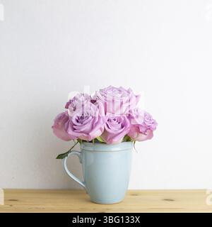 Fleurs roses violettes dans une tasse sur une table en bois avec fond blanc. Espace de copie Banque D'Images