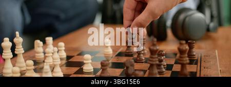 Prise de vue en-tête du site Web d'hommes adultes déplaçant la pièce d'échecs sur l'échiquier en bois pendant le rassemblement d'amis dans le salon Banque D'Images