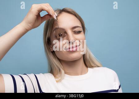 Joyeuse jeune femme heureuse tenant la chaîne de clés de la maison et se réjouit d'acheter de l'immobilier sur fond isolé bleu Banque D'Images