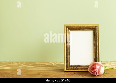 Cadre photo vide avec fleur rose sur table en bois. Fond vert Banque D'Images