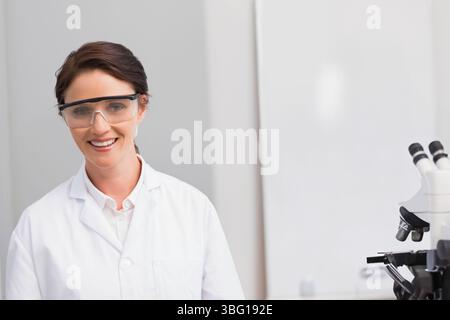 Femme scientifique portant une blouse de laboratoire et des lunettes de sécurité à l'aide d'un microscope composé dans le laboratoire, copiez l'espace Banque D'Images