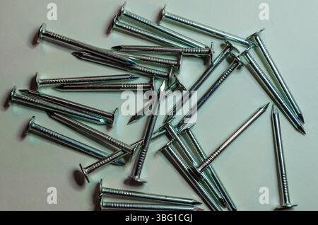Petit groupe de clous de toiture en argent dispersés sur un fond blanc Banque D'Images