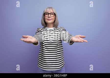 Femme d'affaires d'âge moyen avec les cheveux gris étire amoureusement ses bras pour un câlin sur un fond de studio lumineux Banque D'Images