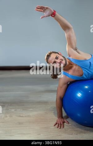 Homme étirant côté sur ballon de stabilité bleu dans la salle de gym à domicile portant un haut athlétique, espace copie Banque D'Images