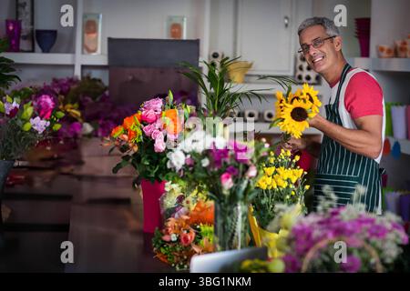 Fleuriste masculin adulte moyen portant tablier arrangeant des bouquets sur le comptoir à la boutique de fleurs, espace copie Banque D'Images
