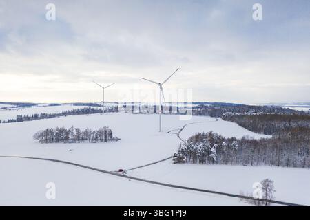 Vue aérienne drone d'un paysage enneigé forêt et champs au coucher du soleil dans la campagne hivernale avec route et deux moulins à vent horizon visible Banque D'Images