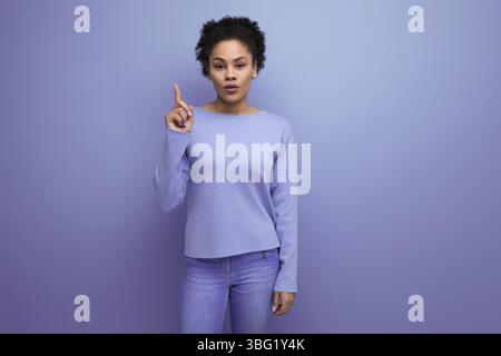 Sérieuse jeune femme latino des années 20 avec les cheveux noirs attachés dans un chignon montre l'idée avec son doigt Banque D'Images