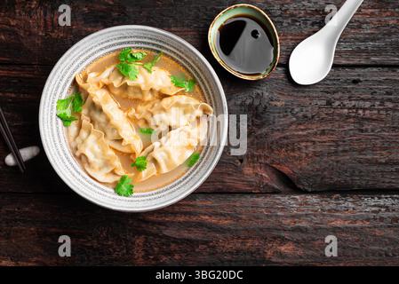 Bol à soupe wonton sur fond de bois foncé, vue de dessus, espace de copie. Soupe wonton de crevettes ou de porc avec ciliantro, vue de dessus. Déjeuner de style asiatique - boulettes donc Banque D'Images