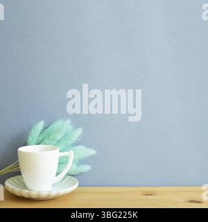 Tasse à café avec herbe sèche Lagurus ovatus sur table en bois. Arrière-plan bleu, espace de copie Banque D'Images